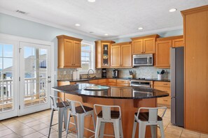 A kitchen with wooden cabinets, a central island with stools, a refrigerator, and a microwave.