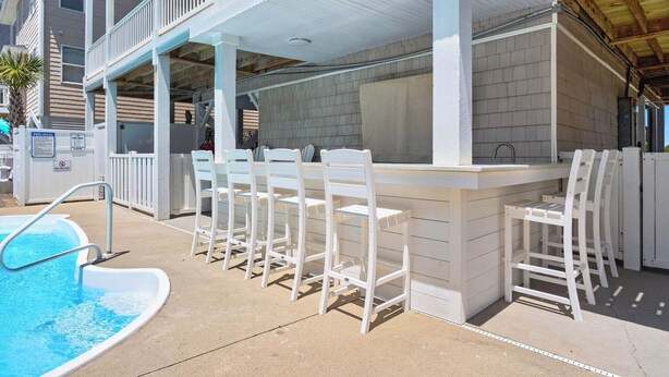 A poolside bar area with white bar stools and a pool. - Spacious 7-bedroom Beach House in fantastic Ocean Isle Beach w/ Private Pool&AC (Ocean Isle Beach)