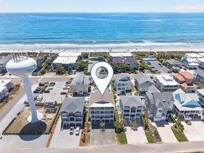 Luchtbeeld van een kustgebied met woningen, een hoge watertoren en een strand op de achtergrond.