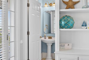 Een badkamer met een witte wastafel op voetstuk, een zeester decoratie, en een bordje met de tekst 'Ocean Isle is my happy place'.