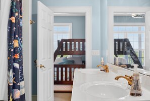 A bedroom with a bunk bed, a bathroom with a large sink and mirror, and a view of the outdoors through the window. - Spacious 7-bedroom Beach House in fantastic Ocean Isle Beach w/ Private Pool&AC (Ocean Isle Beach)
