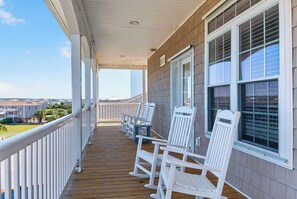 Terraza de madera con mecedoras blancas y vista a un barrio residencial.