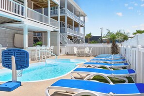A pool area with blue lounge chairs, a basketball hoop, and a multi-level building with balconies. - Spacious 7-bedroom Beach House in fantastic Ocean Isle Beach w/ Private Pool&AC (Ocean Isle Beach)