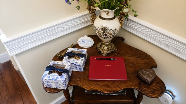 A table with a vase of flowers, a red notebook, and two gift boxes. - Historic 1825 Chesapeake Farm Stay  (St. Leonard)