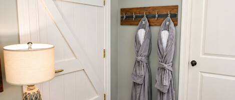 A room with a white door, a wooden coat rack with robes, a lamp, and a bottle on a side table.