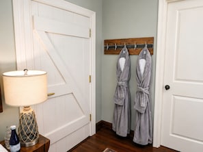A room with a white door, a wooden coat rack with robes, a lamp, and a bottle on a side table. - Historic 1825 Chesapeake Farm Stay (St. Leonard)