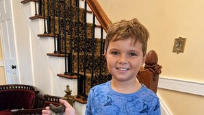 A person holding a shark tooth in a room with a staircase, a red chair, and patterned carpet. - Historic 1825 Chesapeake Farm Stay  (St. Leonard)