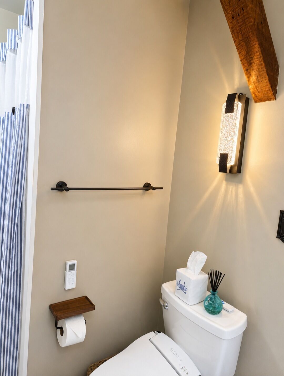 Une salle de bain équipée d’un WC, d’un sèche-mains, d’un distributeur d’essuie-tout, d’un rouleau de papier toilette, d’une boîte de mouchoirs et d’un luminaire fixé au mur.