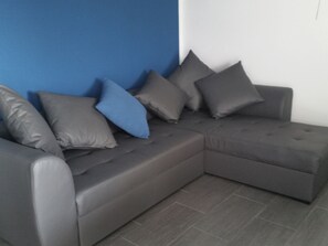 A grey sectional sofa with multiple cushions against a blue wall and grey tiled floor. - Lijepi pogled 2 / HR-10522-02 by Interhome (Vir)