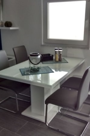 A modern dining area with a glass table, metal chairs, and a window providing natural light. - Lijepi pogled 2 / HR-10522-02 by Interhome (Vir)