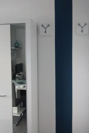 Ein Zimmer mit weißer Tür, blauer Akzentwand und einem Regal mit einer grünen Flasche und einem schwarzen Gegenstand.