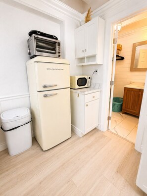 A compact kitchen with a vintage refrigerator, a microwave, and a trash bin. - Sea La Vie, Oceanfront! Free Beach Service! (Panama City Beach)