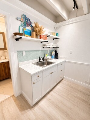 A kitchen with white cabinetry, a marble countertop, a stainless steel sink, and a decorative wall clock. - Sea La Vie, Oceanfront! Free Beach Service! (Panama City Beach)