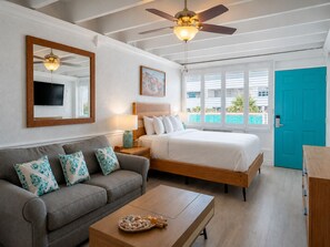 A hotel room with a bed, a sofa, a coffee table, a ceiling fan, a TV, and a door. - Sea La Vie, Oceanfront! Free Beach Service! (Panama City Beach)