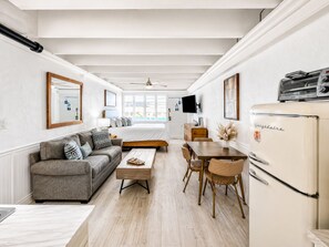 A compact living space with a sofa, coffee table, dining table, chairs, a refrigerator, a TV, and a bed. - Sea La Vie, Oceanfront! Free Beach Service! (Panama City Beach)