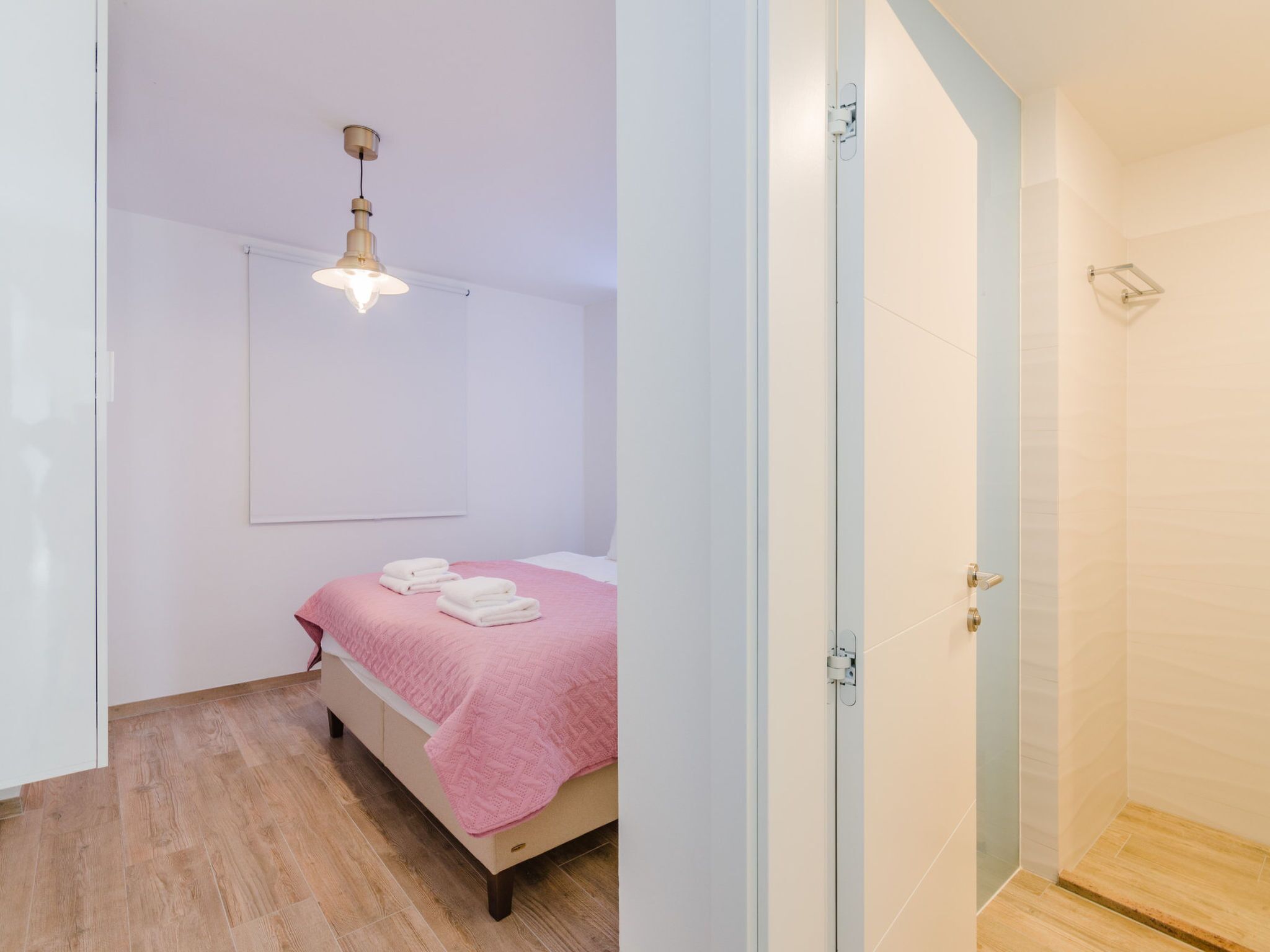 Un dormitorio con una cama, una colcha rosa, una lámpara en el techo y una puerta que da a un baño.