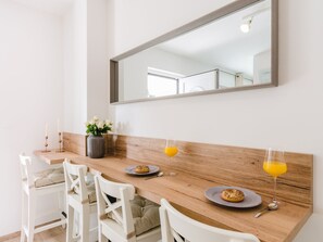Ein Frühstückstisch mit Holz, weißen Stühlen, einer Blumenvase und zwei Gläsern Orangensaft.