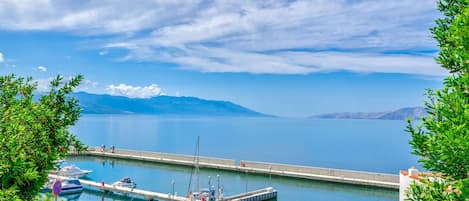 A marina with boats docked, a pier extending into the water, and mountains in the background.