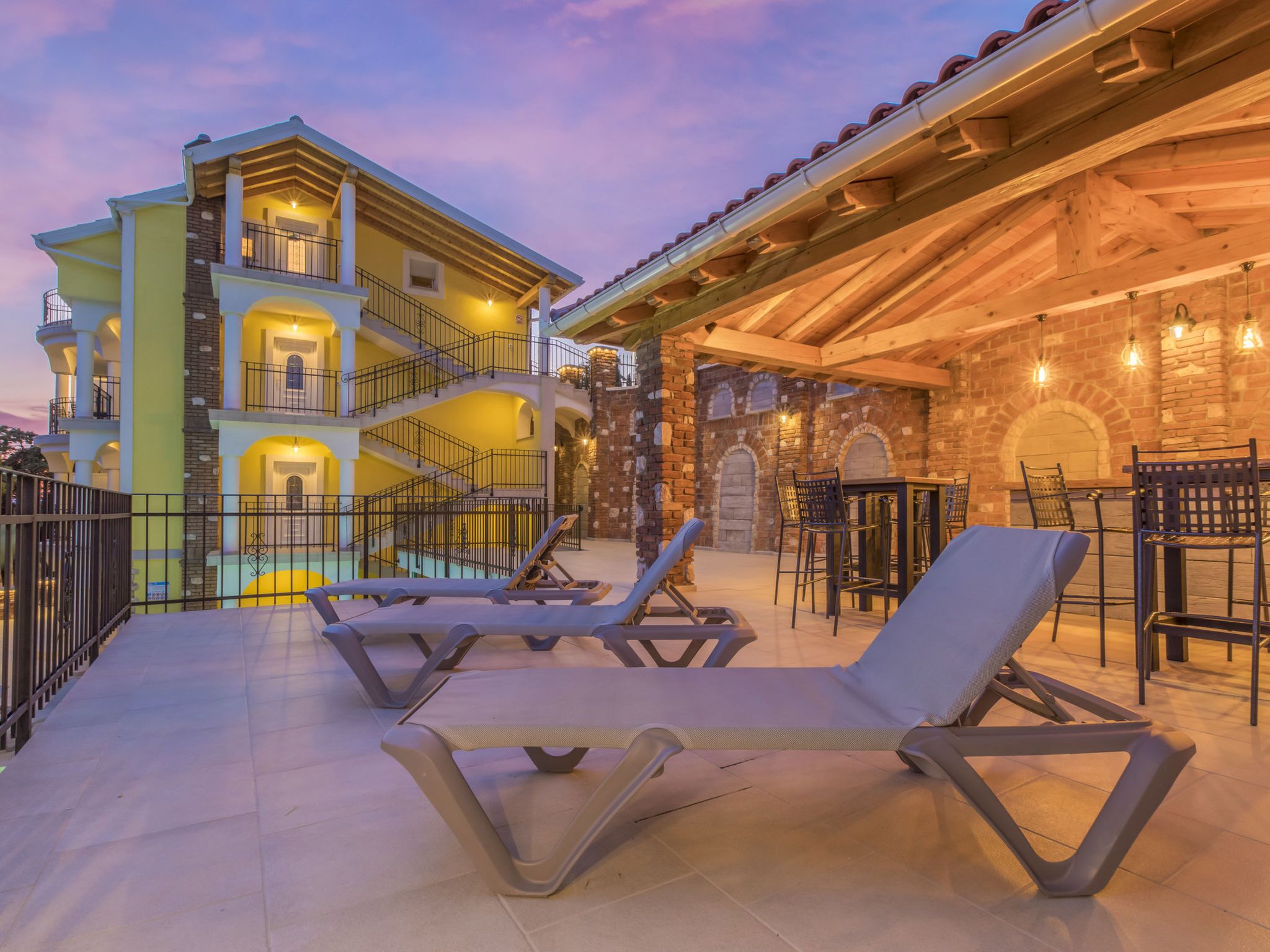 A multi-story building with a pool area, outdoor seating, and a stone facade.