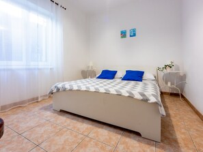 Une chambre à coucher avec un lit, deux tables de chevet, une fenêtre avec des rideaux et un mur orné de deux petits tableaux.