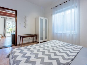Ein Schlafzimmer mit Bett, Kleiderschrank, einem kleinen Tisch und Blick ins Freie.