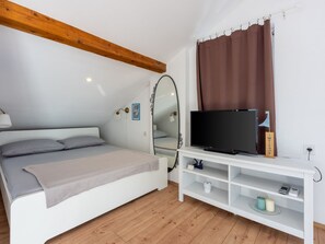 A bedroom with a bed, a TV, a mirror, and a wooden ceiling beam. - Apartmani Zoricic 3 / HR-11028-03 by Interhome (Novi Vinodolski)