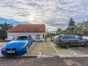 Un estacionamiento con dos coches, un edificio de techo rojo y árboles al fondo.