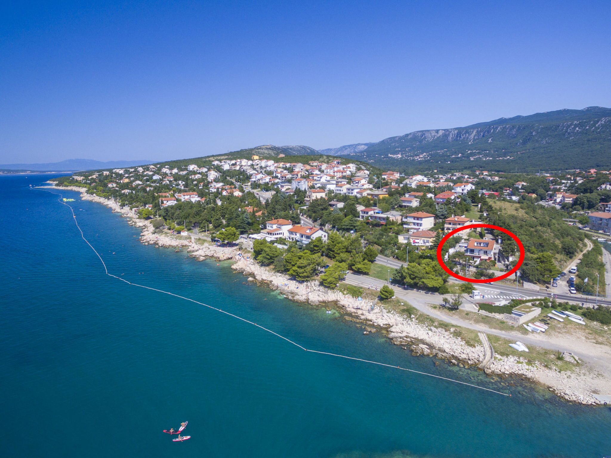 An aerial view of a coastal town with houses, a clear blue sea, and a rocky shoreline.