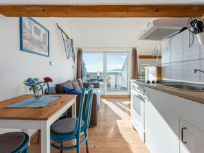 A modern kitchen with a built-in oven, a dining area with a wooden table and blue chairs, and a balcony with a view. - Apartmani Zoricic 3 / HR-11028-03 by Interhome (Novi Vinodolski)