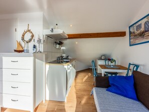 Una cocina compacta con zona de comedor, vigas de madera y un armario blanco.