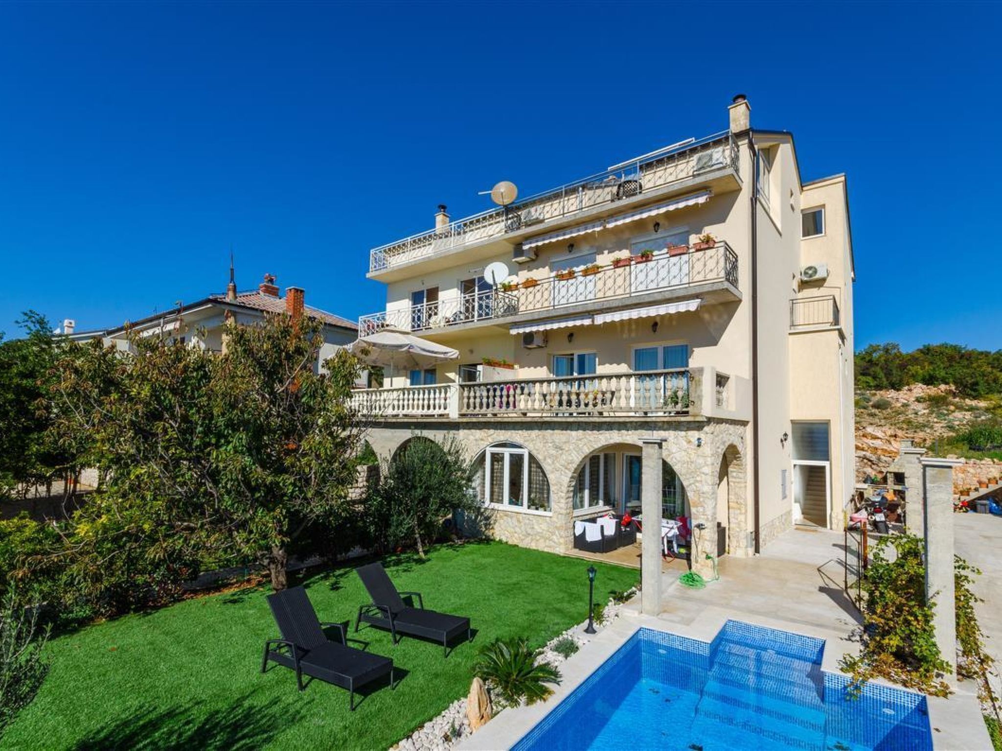 A multi-story building with a swimming pool, outdoor seating, and a well-maintained lawn.