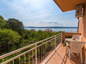Ein Balkon mit Blick auf einen See und sanfte Hügel, weiße Stühle und ein Tisch.
