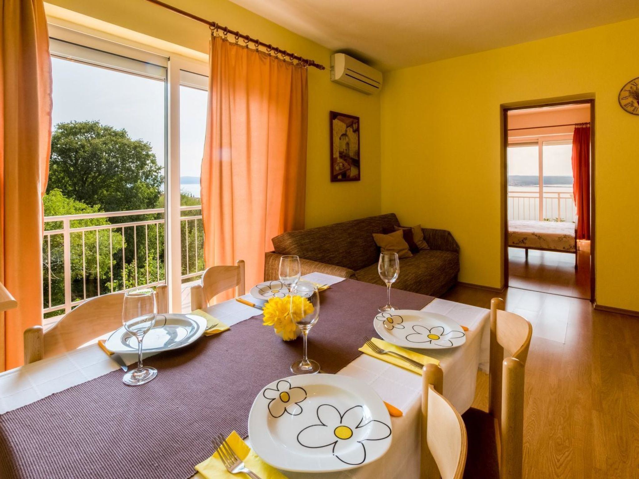 Una zona pranzo con tavolo apparecchiato per due, un divano e un balcone con vista.