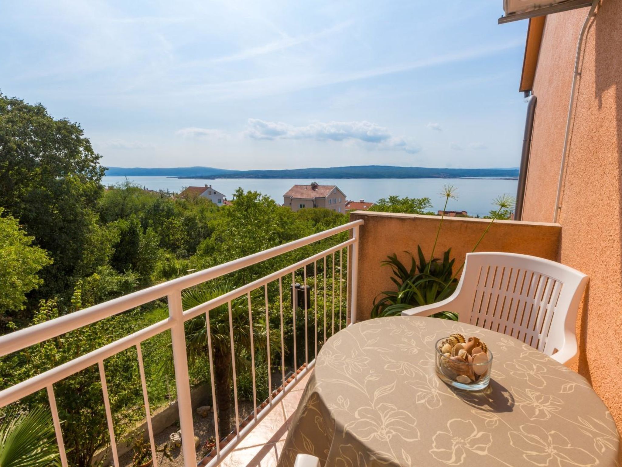 Un balcón con una mesa, una silla y vistas a un lago con edificios al fondo.