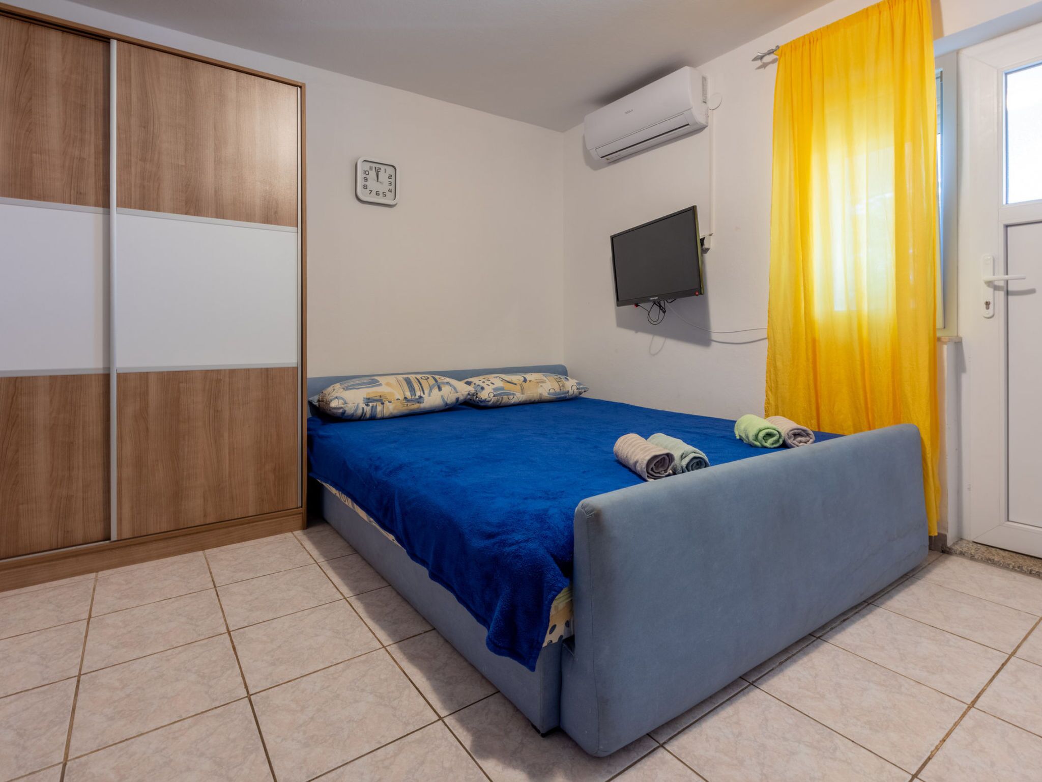 A bedroom with a bed, a TV, an air conditioner, and a wardrobe.