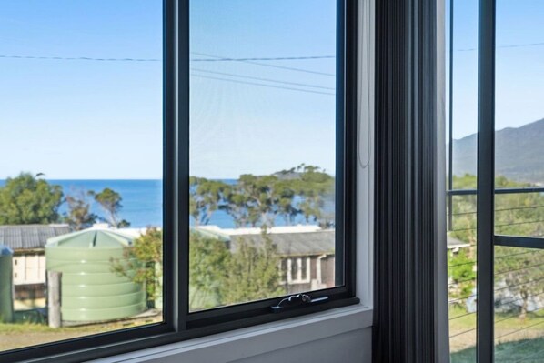 A window with a view of a coastal landscape, including a body of water and greenery.