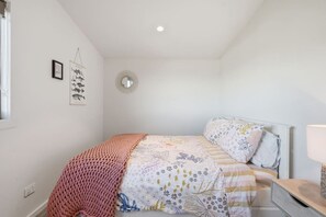 A bedroom with a bed, a bedside table, a lamp, a wall-mounted mirror, and framed pictures.