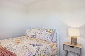 Een slaapkamer met een bed, een nachtkastje met een lamp en een wandplank.