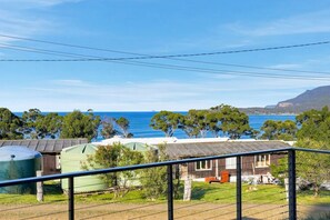 A coastal property with a view of the sea, a fenced area with a green structure, and a wooden building.
