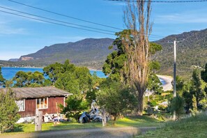 A coastal property with a wooden building, a large tree, and a view of the sea and hills.