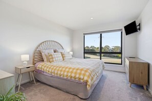 A bedroom with a bed, bedside table, lamp, dresser, and a TV mounted on the wall. - Coastal 2BR Escape, Steps to Beach, Dining and Bar (Eaglehawk Neck)