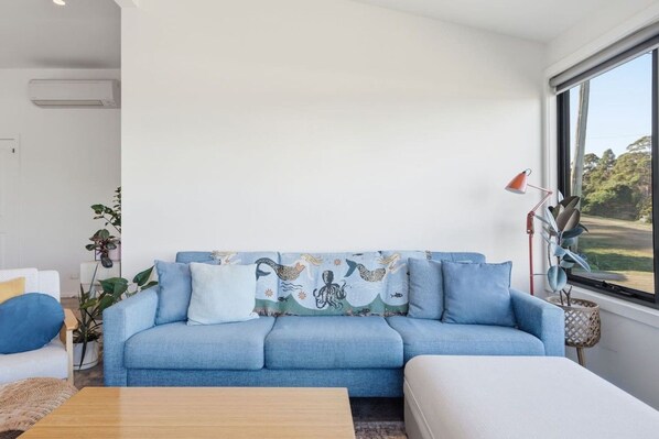 A modern living room with a blue sofa, a coffee table, and a large window with a view of greenery.