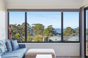 A room with a large window offering a view of the sea and trees.