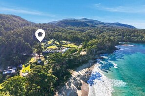 A coastal property with a beach, forested hills, and a clear view of the ocean.