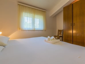 A hotel room with a bed, a window with curtains, a wooden wardrobe, and a chair. - IRIS 4 / HR-02362-04 by Interhome (Crikvenica)