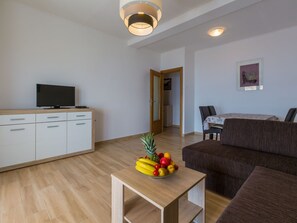 Ein modernes Wohnzimmer mit Fernseher, einem Holzesstisch mit Obst, einem braunen Sofa und einem weißen Schrank.