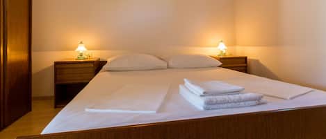 A neatly made bed with white linens and towels, two bedside tables with lamps, and a wooden wardrobe.