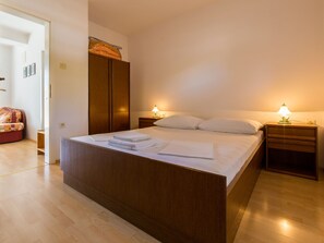 A bedroom with a wooden bed, two bedside tables with lamps, a wardrobe, and a red chair. - IRIS 1 / HR-02362-05 by Interhome (Crikvenica)