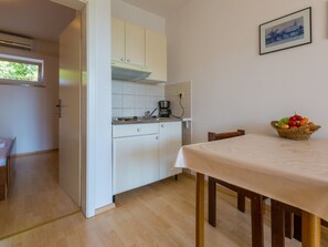 A compact kitchen with white cabinets, a coffee maker, and a dining table with a basket of fruit. - IRIS 1 / HR-02362-05 by Interhome (Crikvenica)