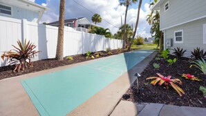 A residential street with a green pavement, white fences, and tropical plants. - The Kove  (Fort Myers Beach)